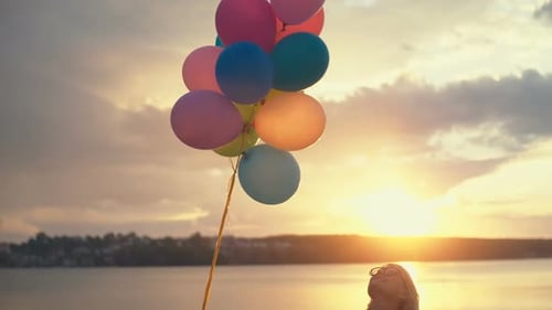 Young Woman with Helium Balloons in Hand Walking on the Beach at Sunset Concept About Birthday and