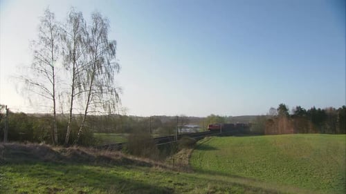 Freight train traveling through a peaceful countryside under a clear blue sky