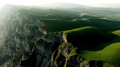 A Rugged Mountain Rises Above a Sprawling Green Landscape Shrouded in Fog and Overlooking a