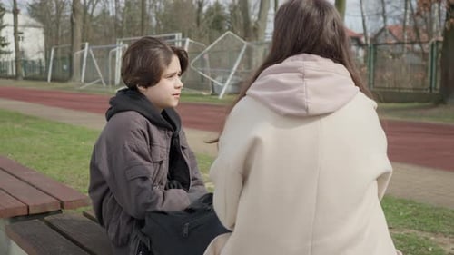 Son talking to his mother, sharing news or feelings after school on a bench