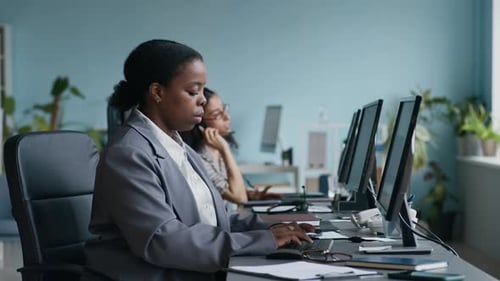 Female Operator Typing and Looking at Computer Screen against Colleague