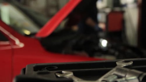 dolly shot on garage with a red car and a professional mechanical doing inspection with soft focus o