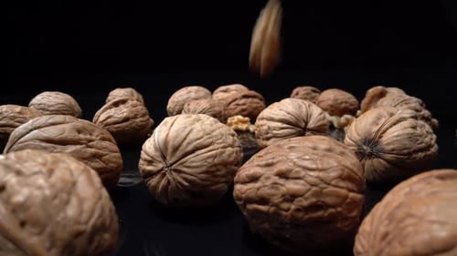 Shelled and Unshelled Walnuts Falling on Black Surface