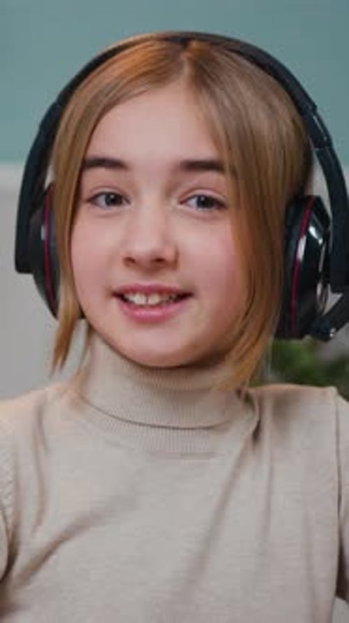 Close Up of Pretty Smiling Little Girl in Headphones Sitting in Front of Laptop Waving Hand While