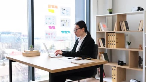 Focused Asian Businesswoman Writing Notes at Modern Office Desk
