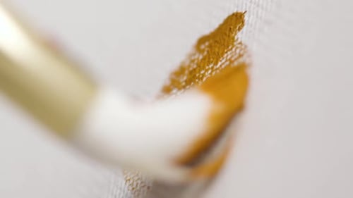 Brush Applying Gold Paint on White Canvas