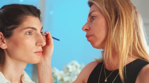 Visagistin trägt im Studio Highlighter auf das Gesicht einer Frau auf
