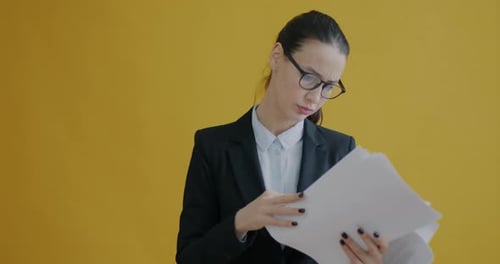 Portrait of Annoyed Businesswoman Reading Documents Then Throwing Papers on Yellow Background