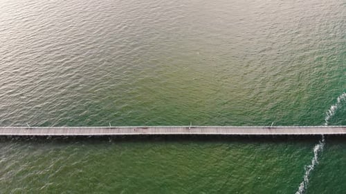High, tilting camera flyover featuring a long, wooden pier that stretches along a vast, deep blue ex