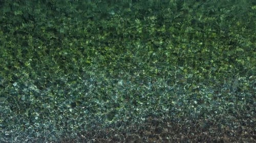 Top view of transparent water sea with stone and pebbles bottom. Sun glare on the surface crystal