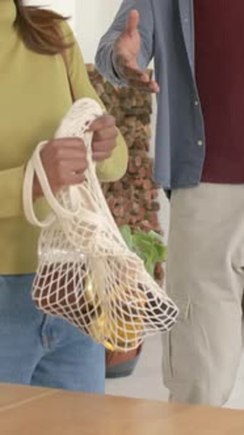 Vídeo vertical: Una mujer entra con una bolsa de malla en su casa, un hombre lleva una bolsa de una planta para dejar las bolsas