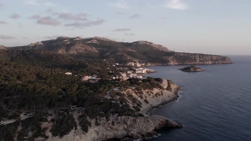 Aerial view of coastal town with cliffs and mountains at sunset, Spain.
