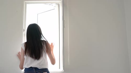 Woman Opens Window in Bright, White Room