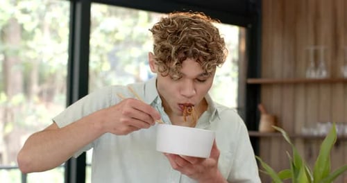Young Adult Eating Noodles with Chopsticks Indoors