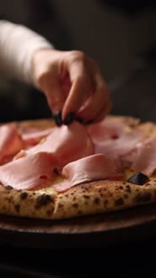 Hand placing ham onto a fresh pizza