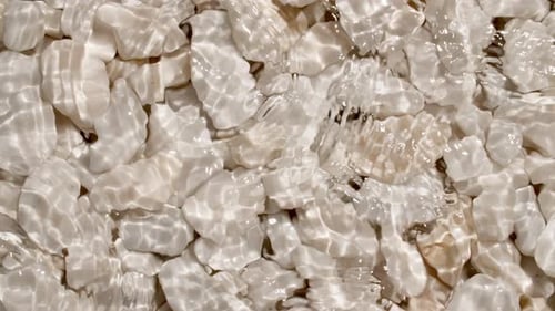 Sea Waves On Pebbles From the Beach Close Up Pure Water with Reflections Sunlight in Slow Motion