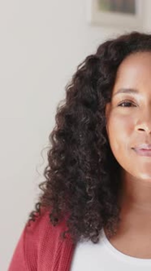 Vertical video of half face of happy biracial woman standing and smiling in sunny house