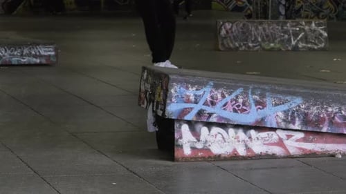 Skateboarder does a boardslide on concrete while people are skateboarding in the skate park Southban