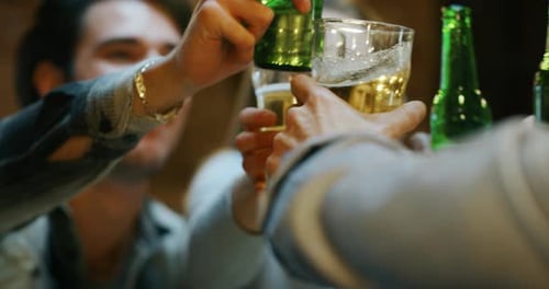 Slow motion close up of happy young friends having fun together drinking beer and clinking glasses