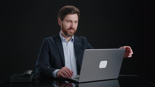 Ein Mann in einem schwarzen Anzug, der an seinem Laptop arbeitet und ihn dann mit einem Lächeln schließt
