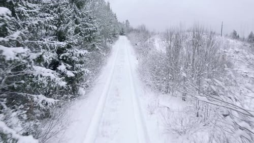 Fly over snow covered small forest road