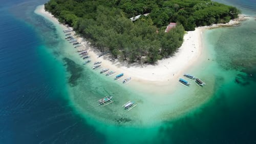 Aerial drone tilt down shot as a jukung traditional boat arrives to a white sand beach with tourists