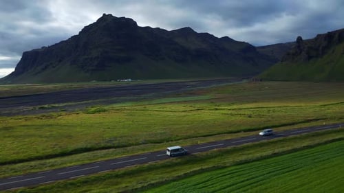 Vehicles Driving On The Road In Iceland With Rocky Mountain In Background. aerial