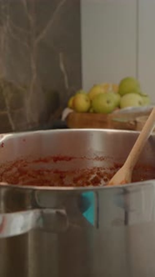 Vertikales Video: Frau rührt kochende Pflaumenmarmelade in einem Edelstahltopf auf der Theke um
