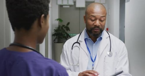 African american male and female doctors using tablet, talking at hospital