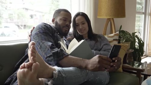 Couple reading book, using smartphone on green couch