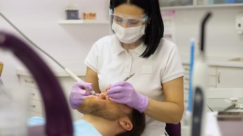Woman Dentist in Face Mask and Glasses Doing Treatment for Male Patient Holding Dental Tools Wearing
