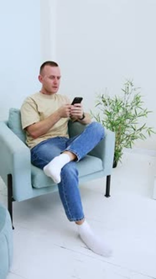 Glücklich lächelnder Mann sitzt auf dem Stuhl und hält sein Handy.