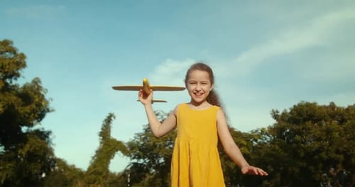 Una niña corre en el parque al otro lado del campo, juega con un avión de juguete en la mano y una silueta en