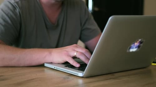 Male hands typing on keyboard laptop lying on wooden table, close-up side view.