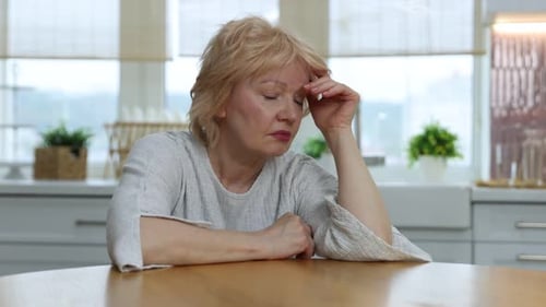 Tired senior woman at table in kitchen
