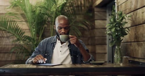 Handsome young man drinking coffee and working on a digital tablet at a cafe