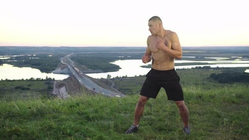 A Muscular Shirtless Man Training Martial Arts on the Hill Above the Highway