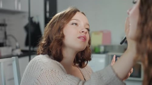Woman Applying Makeup to Friend in Kitchen