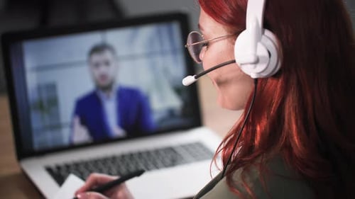 Woman in Headphones on Video Call Taking Notes