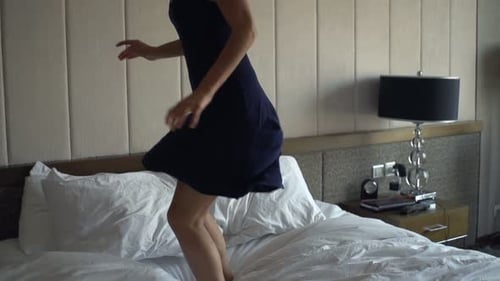 Happy young woman jumping on bed in slow motion at home enjoying her day