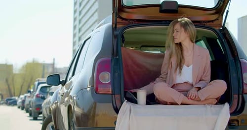 Woman Meditating in Car Trunk in Urban Setting