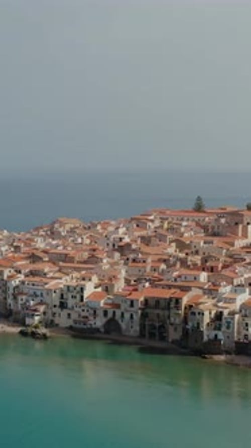 Vertical descending aerial drone shot into the bay of Cefalu town. Sandy beach in a small historic t