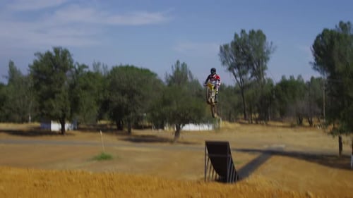 Dirt Bike Rider Jumps Ramp in Rural Outdoor Setting