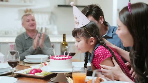 Girl Blowing Out Birthday Candles with Family