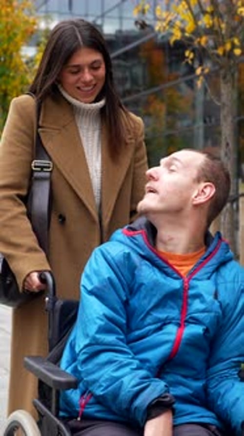 Woman Pushes Man in Wheelchair Through City