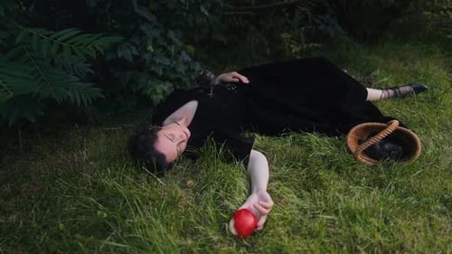 Uma mulher em um vestido preto encontra-se graciosamente na grama verde segurando uma maçã vermelha em uma floresta encantada