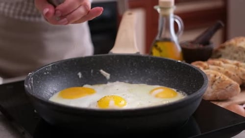 Hands Seasoning Fried Eggs in a Pan