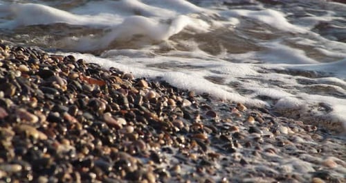 Sea beach of pebbles washed by foam waves in slow motion, static, day