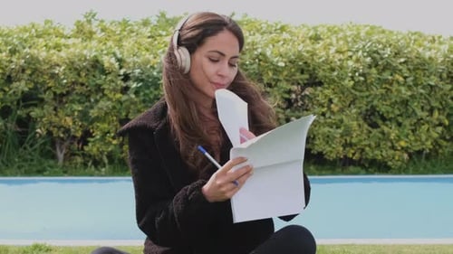Beautiful young woman listening music and studying at the park