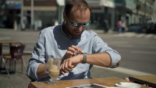 Young man tapping smartwatch screen in sunny cafe in european city